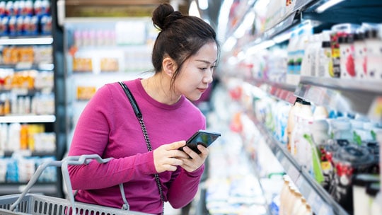 Woman browses groceries with phone in hand.